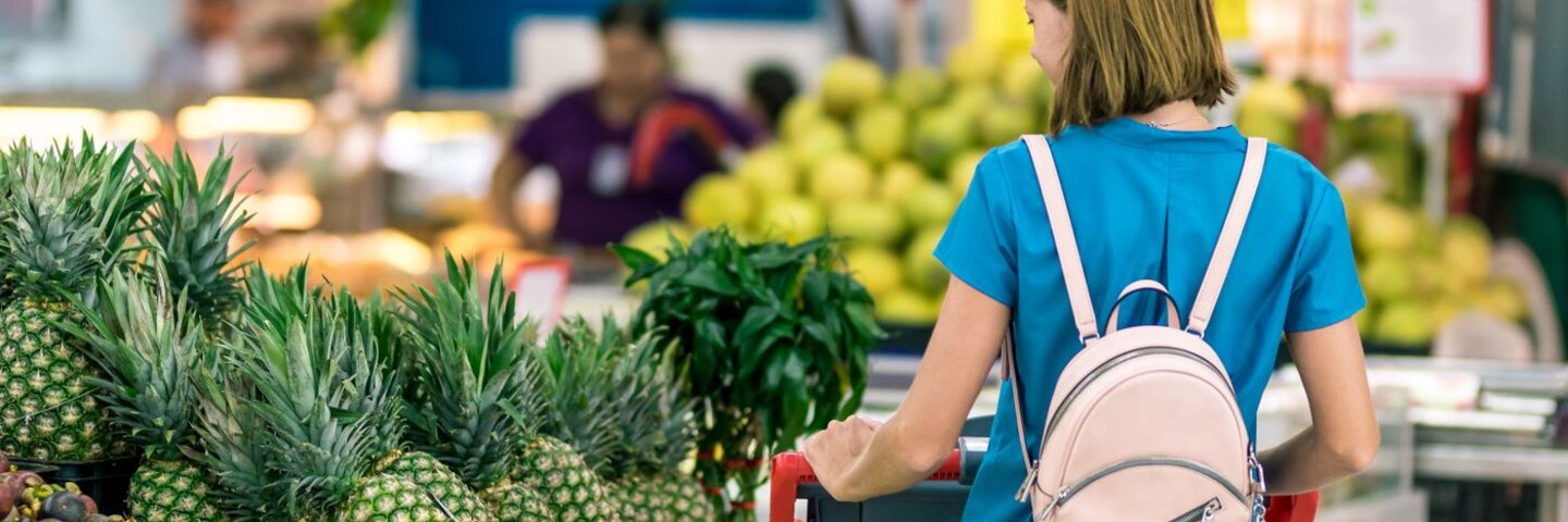 Shopper pushing a cart through a grocery produce aisle