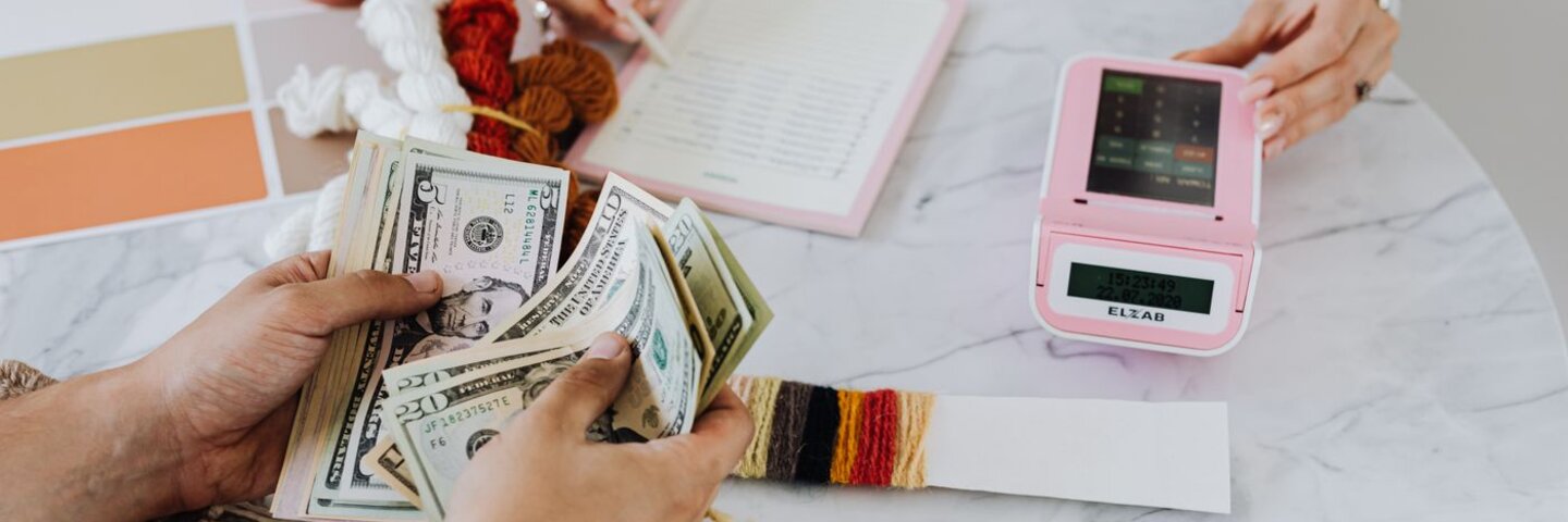 Hands counting cash beside a small-business register