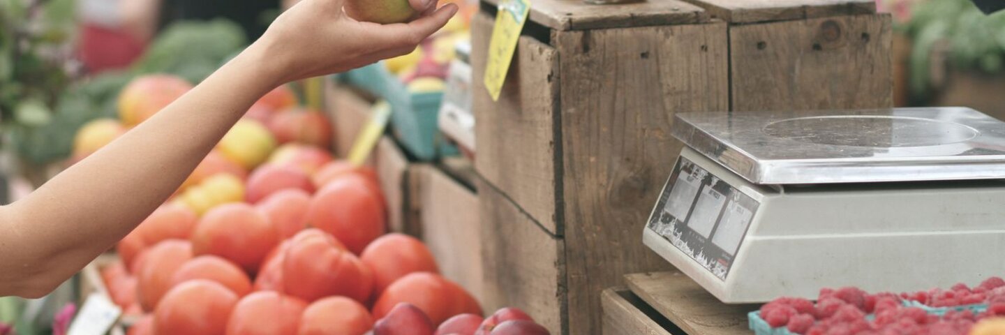 Produce stall with a hand passing a piece of fruit